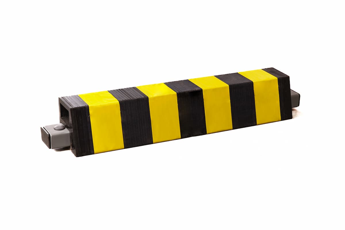 Protección fijada al suelo, con fijaciones metálicas y recubierta de caucho. En color amarillo y negro.